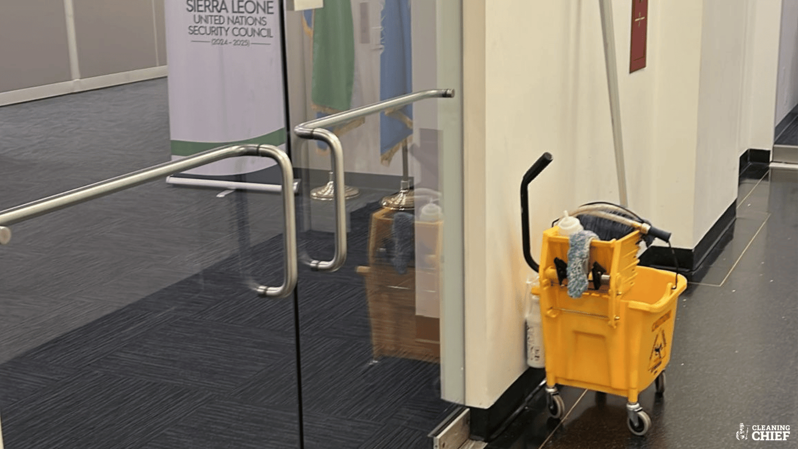 Office cleaning in progress with a mop bucket, cleaning sprays, and supplies placed near a sparkling clean office floor.