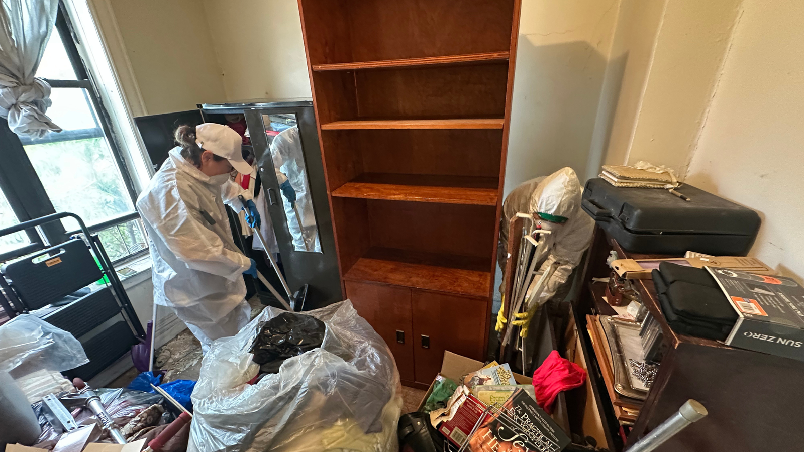 Two professional cleaners in protective suits organizing and decluttering a severely hoarded apartmentâ€